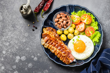 Fried egg, beans, tomatoes, olives and beans on dark background. Top view, copy space.