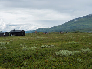 Lapland landscape at Virihaure lake with sami village Arasluokta houses, snow capped mountains and plain with shrubs. Sweden summer moody and foggy wild nature, Padjelantaleden hiking trail.