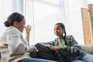 blurred african american woman gesturing while talking to smiling teenage daughter