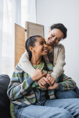 Fototapeta premium happy african american woman embracing teenage daughter sitting on couch at home