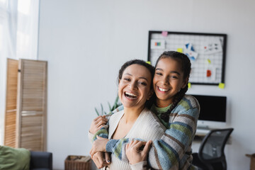 excited african american girl embracing mother while looking at camera