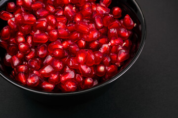 Ripe Pomegranate seeds in black bowl on black background