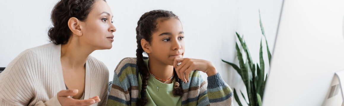 african american woman pointing at computer monitor near thoughtful daughter, banner