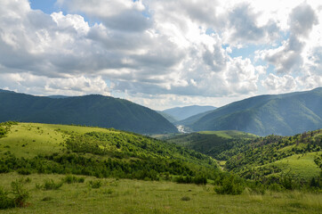 Rural landscape with green mountains covered with forest, grassy meadows, river and village. Carpathian, Ukraine.