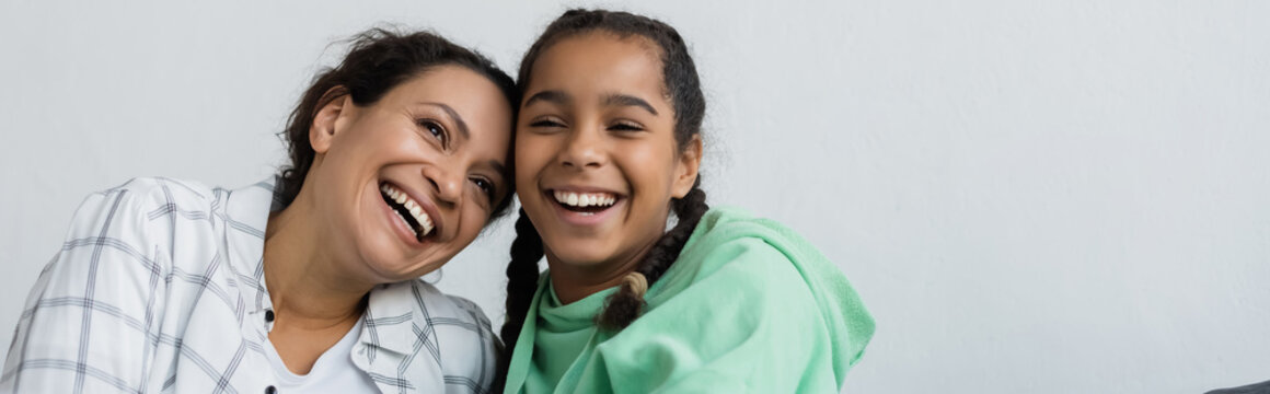 excited african american woman with teenage daughter laughing while spending time at home, banner