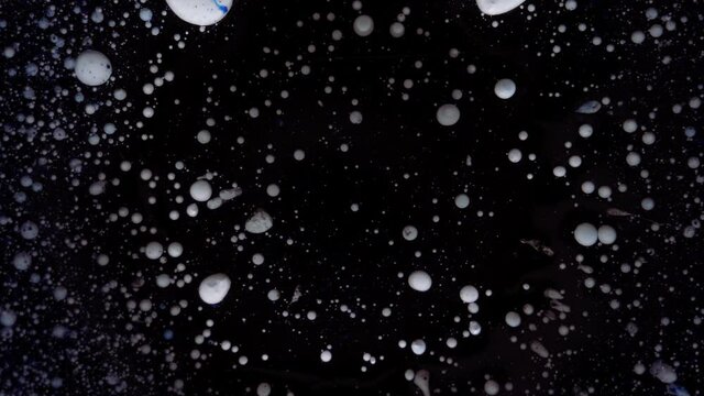 White particles move randomly. Christmas, New Year's screensaver. Round multicolored balls on a black background with silver sequins.