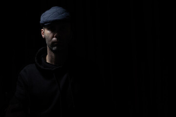 man in kepi and black hoodie is staying in darkness, light and shadows on his face 