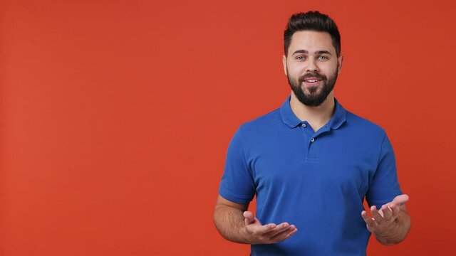 Promoter attractive young bearded brunet man 20s wears blue t-shirt speak tell explain gesticulate with hands pointing finger aside on workspace isolated on plain red orange background studio portrait
