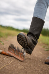 Step on the same rake. A man in kirza boots steps on a sharp metal rake.