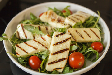 Traditional greek fried halloumi cheese on a white plate with herbs and cherry tomatoes. View from above.