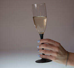 Photo of a woman's hand with a glass of wine, isolated on a light beige backlit background.