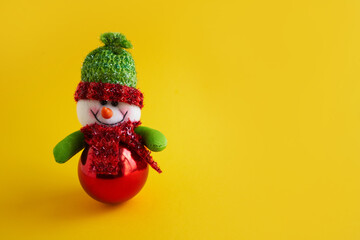 winter holiday concept snowman in a christmas hat and scarf christmas toy on a yellow background place for text