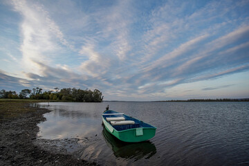                   A small green boat is moored by the lake. The boat is empty, there is no one in it, and there are small ripples on the surface of the water.