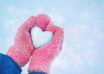 Female hands in knitted mittens with heart of snow on bokeh background. Love concept. Valentine day concept.	