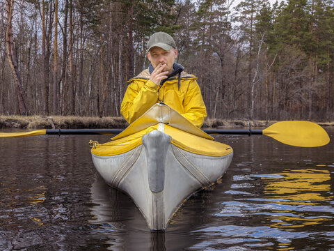 Front view portrait of relaxed smoking cigarette kayaker in yellow jacket on river landscape