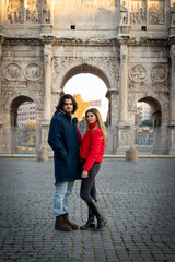 Fototapeta na wymiar Young couple traveling to Rome. The young couple poses in front of the Arch of Titus. The blonde woman in her red jacket puts her hand on her boyfriend.