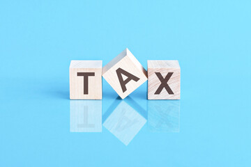 word tax from wooden blocks with letters, front view on blue background. Tax concept with wooden block.