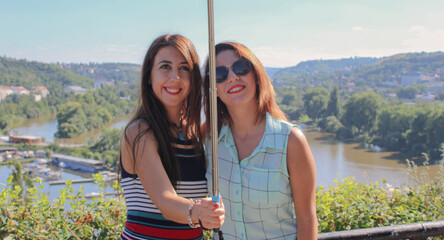 Two friends together happily taking selfie with selfie stick outdoors in tourist park in Prague. Travel concept capturing moments. Copy Space.