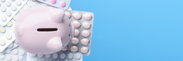 Pink piggy Bank with pills in a blister pack on blue background. Coronavirus, 2019-nCoV. Medicine and healthcare concept. Banner