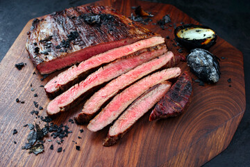 Traditional barbecue wagyu gourmet flank steak with charred onions served as close-up on a modern design wooden board
