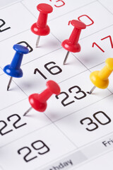 Colored push pins on monthly calendar page. Calendar appointments. Multicolored push pins on...