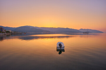 La montagne et le bateau à moteur solitaire reflètent le lever du soleil dans une mer calme, Marmaris
