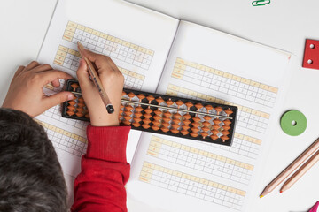 Doing mental math or mental arithmetic. Hand of little boy using abacus for calculating. Learning to use abacus on mental math courses. A kid doing math at home with abacus