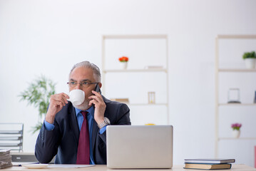 Old male employee having breakfast in the office