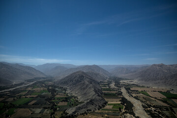 View of andean farmland with mountains and blue sky behind from small passenger plane taking...