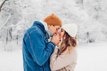 Man warming hands of woman with his breath in snowy cold winter park. Loving couple walking outdoors