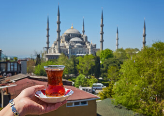 Naklejka premium Woman's hand holding cup with Traditional turkish tea in front of Blue mosque aka Sultanahmet Camii in Istanbul, Turkey.
