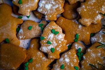 Cookies are on a plate of different shapes, in the foreground there is a cookie in the form of a Christmas tree, decorated with powdered sugar like snow and small green Christmas trees against the