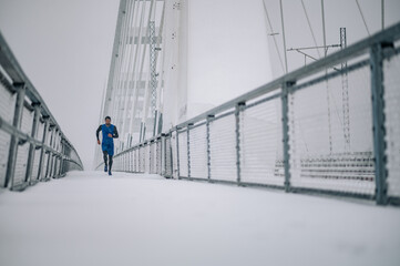 Man running on bridge during a winter snow day.