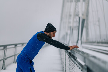 Man stretching before training on bridge during a winter snow day.