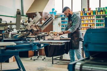Male worker pressing ink on frame while using the printing machine in a workshop