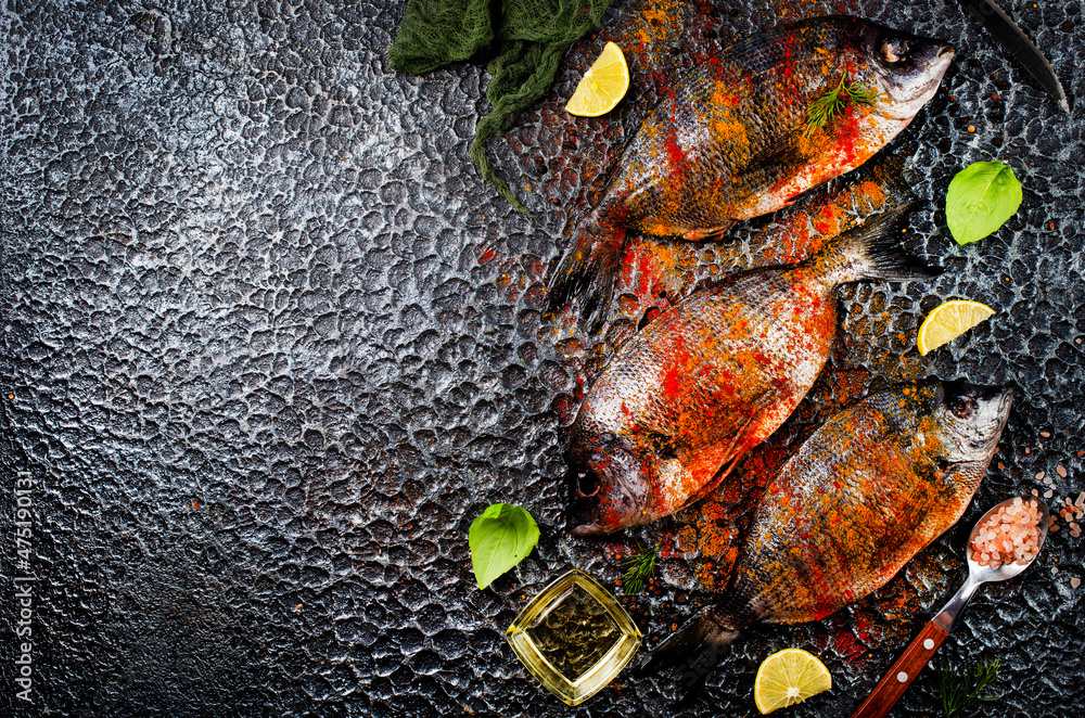 Wall mural Raw fish with herbs, lemon and olive oil on dark textured background.