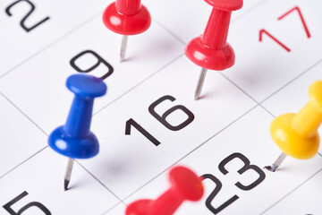 Colored push pins on monthly calendar page. Calendar appointments. Multicolored push pins on calendar. Marked event day, business appointment, meeting with pin. Close-up of push pins on calendar date