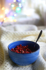 Blue ceramic bowl with fresh pomegranate seeds, soft knitted blanket and colorful bokeh lights. Hygge at home. Selective focus.