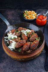 Traditionelle kroatische Cevapi als würzige Fleischbällchen mit scharfem Ajvar und Kraut Karotten Salat serviert als close-up in einer rustikalen Bratpfanne 