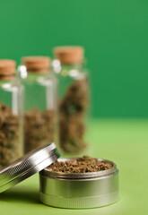 marijuana on grinder, glass jars on table, with dark green background.