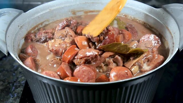 Typical Brazilian feijoada boiling in the rustic pot in close-up