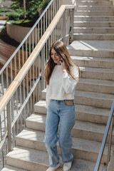 Beautiful stylish woman going down the street stairs on a summer day and holding a mobile phone while talking on it. Smartphone for communication with people. Technologies of the present.