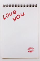 the words I love you and a trace of red lipstick on a white background of a notebook sheet on a spring