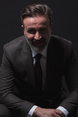 Fototapeta premium Portrait of adult businessman wearing trendy suit and sitting in modern studio on stylish chair against the black background