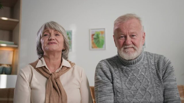 senior aged couple using laptop computer, smiling grandparents nod their heads together and waving hands on camera