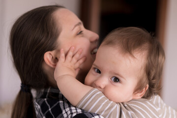 Portrait Adorable Face Of Little Cheerful Happy Toddler baby girl child With Charming Smile Look At Mom Strong Cuddles Loving Mommy Together. Mother Hugs play love care kiss smiling daughter at home