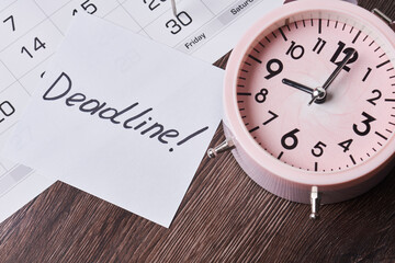 Deadline text on piece of paper, alarm clock and monthly calendar on the desk. White card with Deadline text and last date of month with dart pin on calendar date. Last day, Last chance concepts