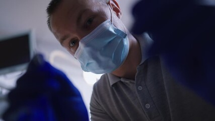 Portrait of concentrated professional male dentist with mouth mirror and dental probe in dental clinic working. Patient point of view Caucasian expert orthodontist examining teeth in slow motion