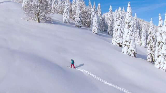 AERIAL Young female tourist snowshoes up a snowy hill during a snowboarding trip