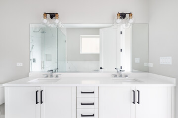 A modern, white luxury bathroom with black hardware and chrome faucets. A large glass walled shower sits in the corner with marble tiles from floor to ceiling.